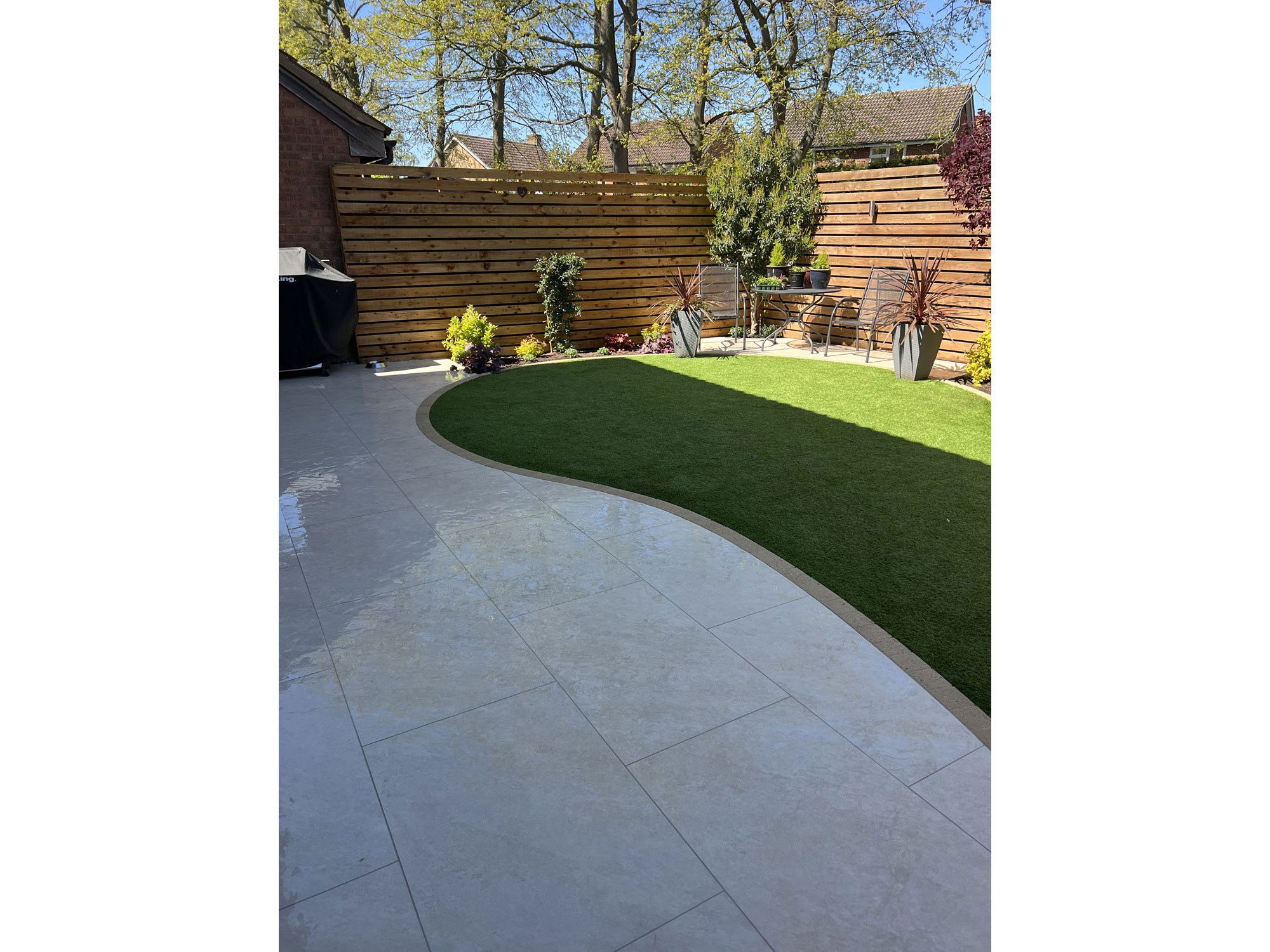 Curved Millboard composite decking and porcelain paving in a landscaped garden