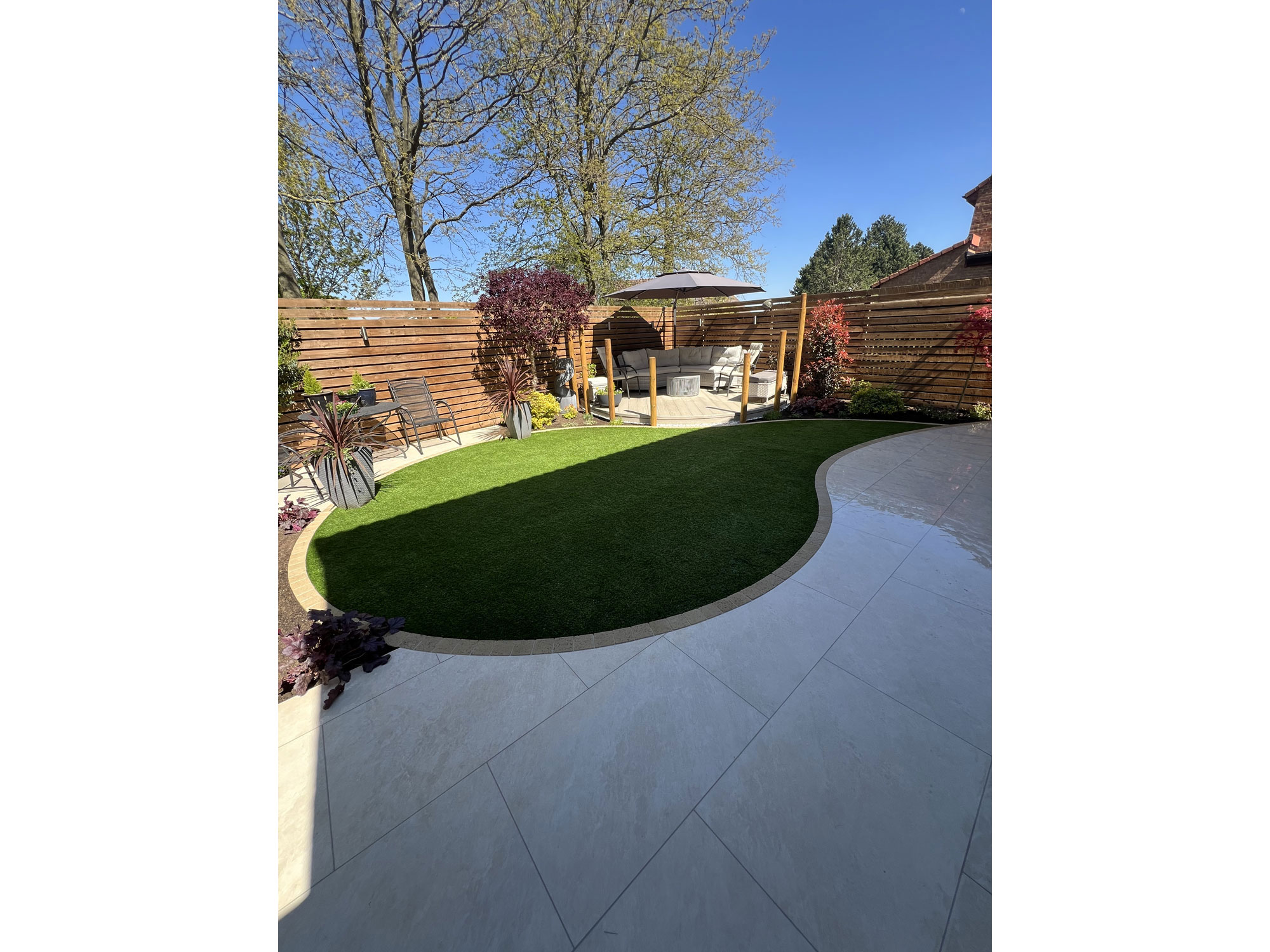 Circular composite decking and curved porcelain paving creating distinct garden seating areas