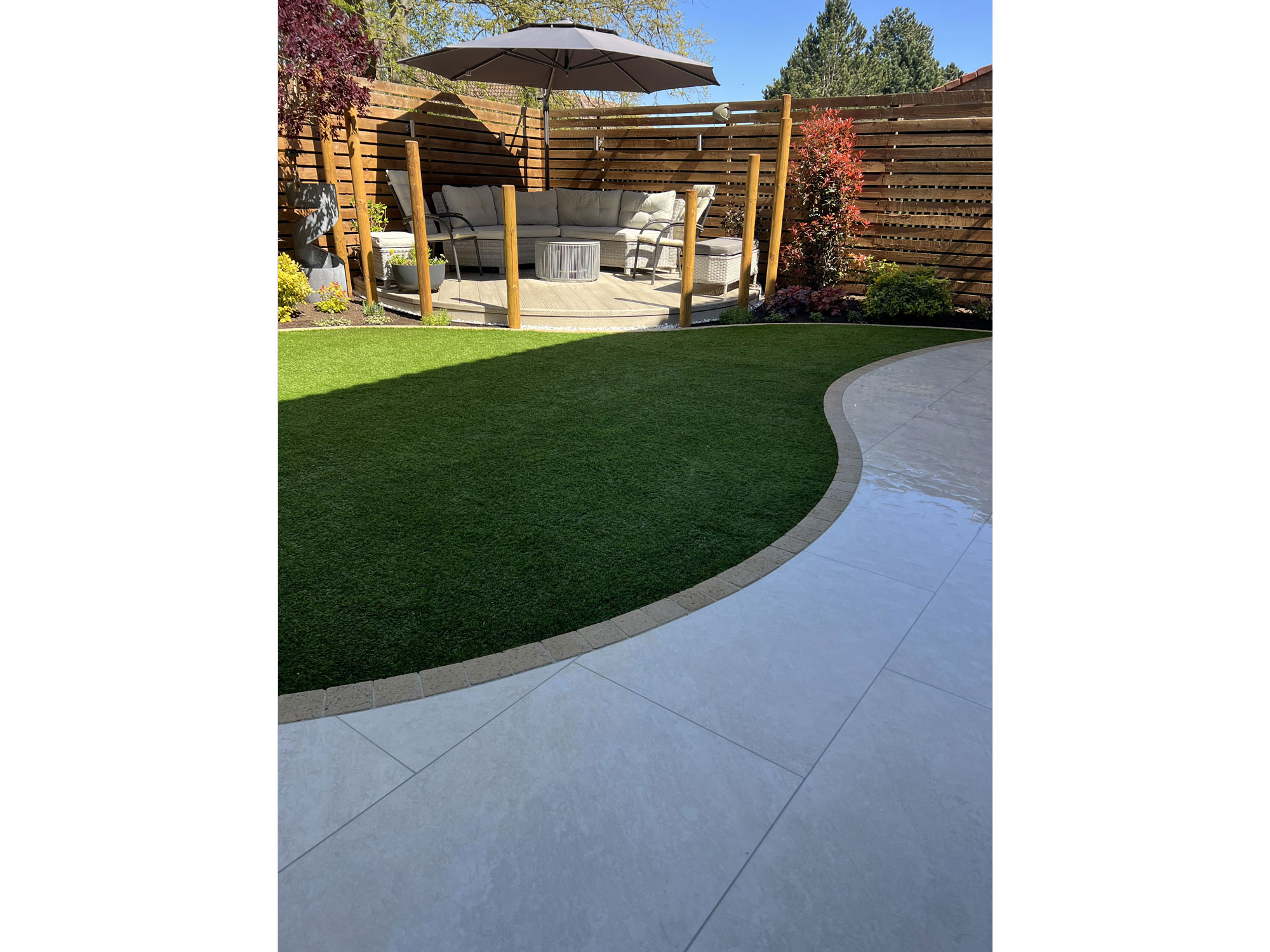Circular Millboard decking surrounded by curved porcelain paving and bespoke garden features