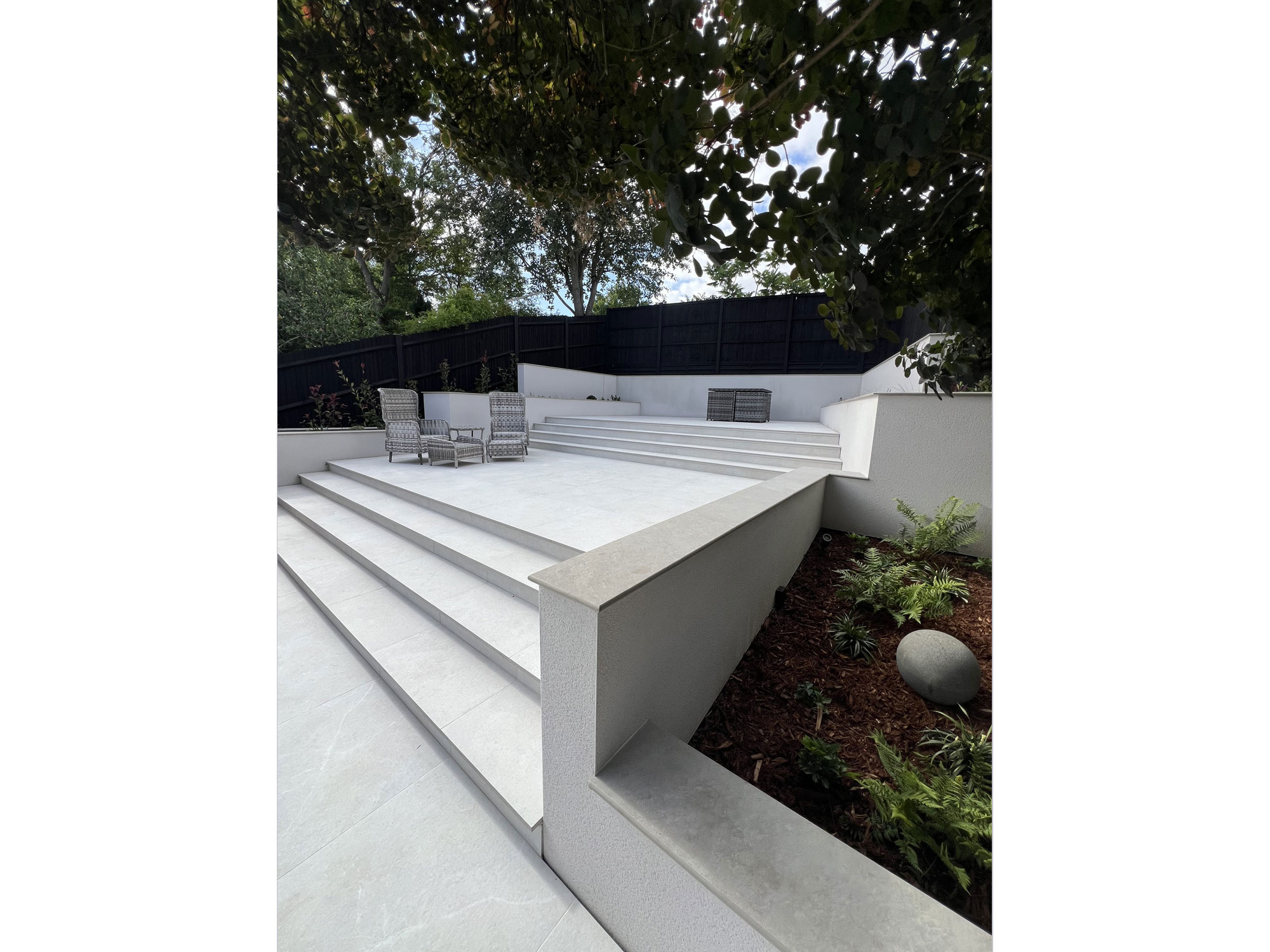 Stylish tiered garden design with porcelain paving, rendered planters and planting